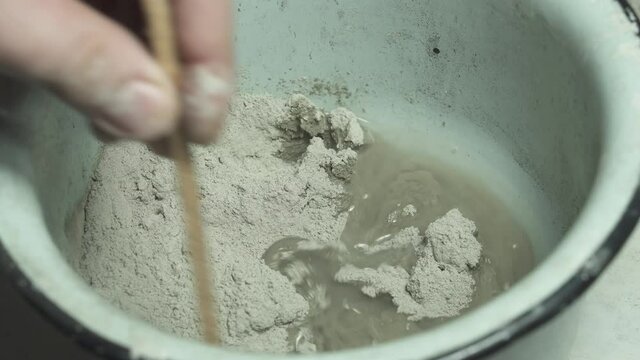 Man is mixing spackling paste putty in the bucket. Grind of wall. Maintenance repair works renovation in the flat. Restoration indoors. Concrete background.