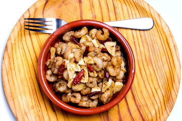 Prawns with garlic and cayenne in a ceramic bowl on a wooden tray