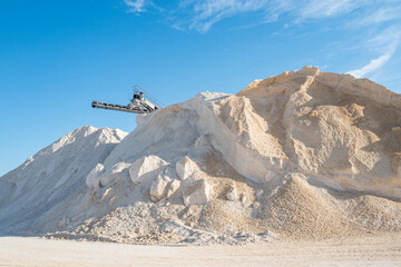 Stone crushing conveyor belt equipment and huge piles of crushed limestone against a blue sky in...