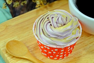 Homemade cupcake served on wooden cutting board with a cup of black coffee and wooden spoon on wooden table.