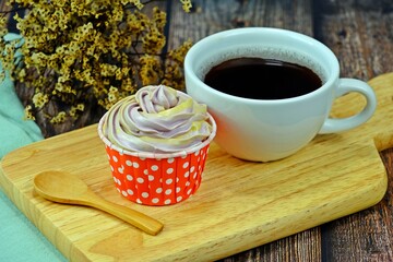 Homemade cupcake served on wooden cutting board with a cup of black coffee and wooden spoon on wooden table.