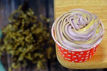 Homemade cupcake on the rim of wooden table with blurred dried flowers background.