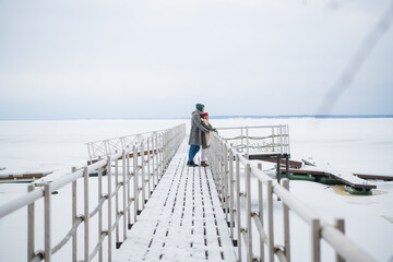 Lovers warm each other with love and hugs on a winter walk along the pier on the lake.