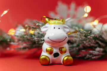 Merry Christmas and happy new year. Festive composition. Symbol of the year 2021 bull with a new year and christmas fir branch, white snowflake and garland on red background