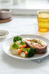 Steam salmon and vegetables, Paleo, keto, fodmap, dash diet. Side view, vertical. Mediterranean diet with steamed fish. Healthy concept, white plate on gray table, gluten free, lectine free