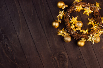 Fototapeta na wymiar Fashion festive christmas background - wreath, golden glossy and glitter balls, glowing stars on dark brown wood board, border, top view.