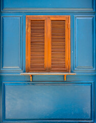 Traditional wooden casement window with slat blinds on blue wall. Exterior decoration of classic Italian style.