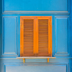 Closeup of traditional wooden casement window with slat blinds on blue wall. Exterior decoration of classic Italian style.