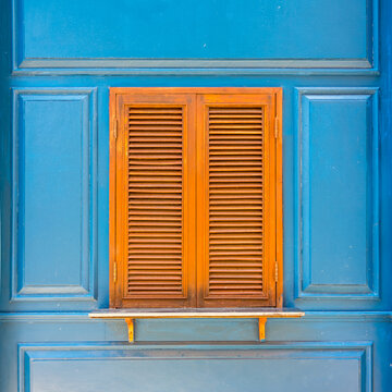 Closeup of traditional wooden casement window with slat blinds on blue wall. Exterior decoration of classic Italian style.