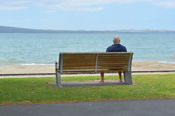 View of man sitting on bench and looking at sea
