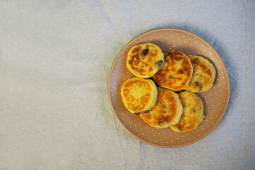 six yellow sugar-free cheesecakes with banana and raisins in cornmeal lie in a brown round plate with polka dots on a gray tablecloth top view . cooking gluten-free cheesecakes at home