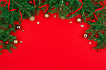 Top view of Christmas frame made of fir tree, golden decorations, confetti, snowflakes on red background with copy space. © greola84
