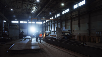 Obraz premium Two Heavy Industry Engineers Walk in Steel Metal Manufacturing Factory, Use Digital Tablet Computer and Have a Discussion. Black African American Industrial Specialist Talk to Female Technician.