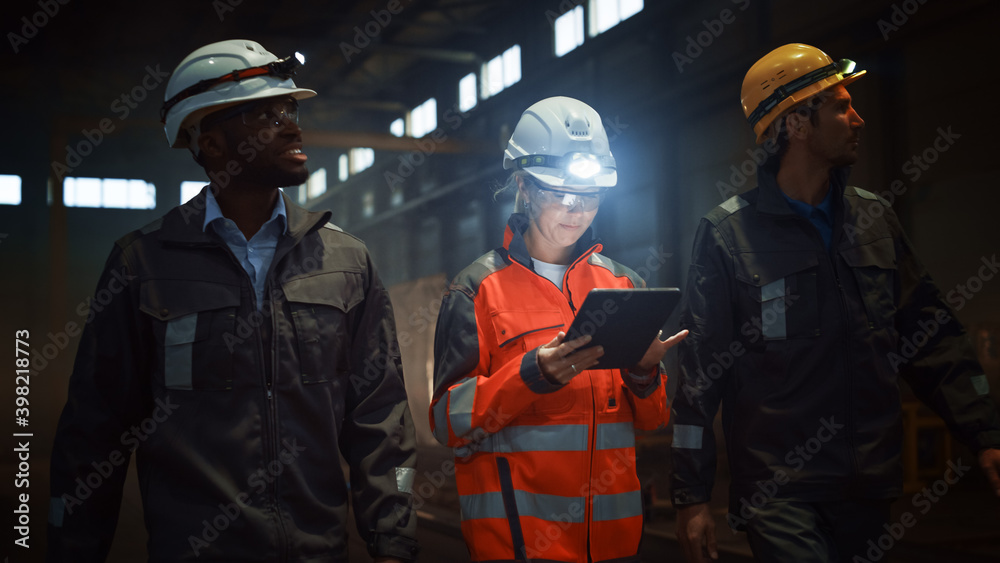 Leinwandbilder three diverse multicultural heavy industry engineers and workers in uniform walk in dark steel facto