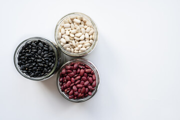 glass jar with black bean, red kidney bean and white bean. navy, cannelini, white kidney bean on white background. triangle shape made from beans jar isolated top view photo