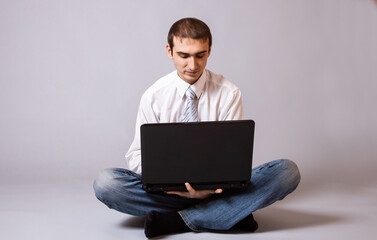 Photo of adult european man in business clothing sitting on floor  and working on black laptop