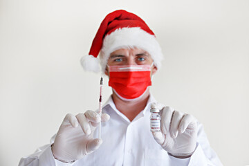 Coronavirus vaccine as christmas present concept. Portrait of a doctor wearing Santa's hat, red face mask and latex gloves demonstrating new covid-19 vaccine in vial. Close up, copy space, background.