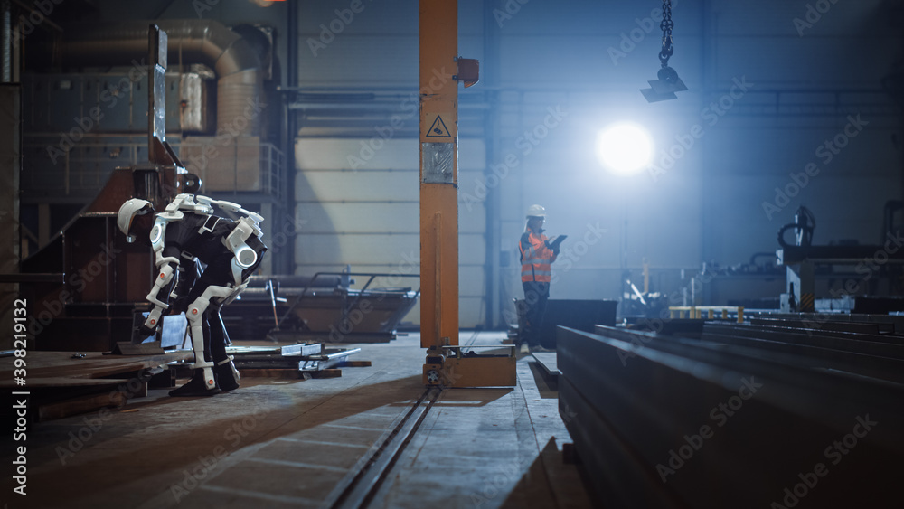 Poster Black African American Engineer is Testing a Futuristic Bionic Exoskeleton and Picking Up Metal Objects in a Heavy Steel Industry Factory. Contractor is Heavy Lifting Steel Parts in a Powered Shell.