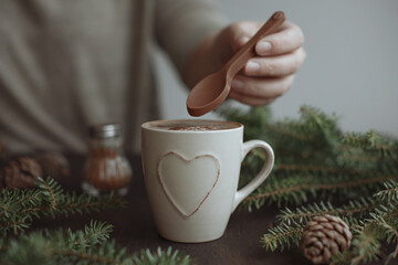 A woman prepares Christmas coffee with cinnamon. Spruce branches and cones, chocolate spoon. Winter mood.