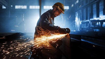 Heavy Industry Engineering Factory Interior with Industrial Worker Using Angle Grinder and Cutting a Metal Tube. Contractor in Safety Uniform and Hard Hat Manufacturing Metal Structures. - obrazy, fototapety, plakaty