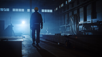 Professional Heavy Industry Engineer/Worker Wearing Uniform, Glasses and Hard Hat in a Steel Factory. Industrial Specialist Walking Away in a Dark Metal Construction Manufacture.
