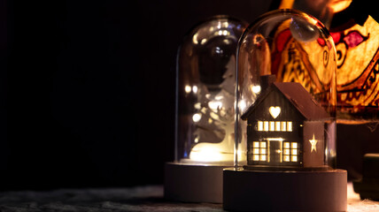 Fototapeta na wymiar Little wooden house with warm lights inside a glass bell. Christmas decoration. Dark Background.