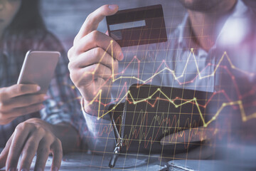 Double exposure of man and woman on-line shopping holding a credit card and forex graph hologram drawing. Stock market E-commerce pay on-line concept.