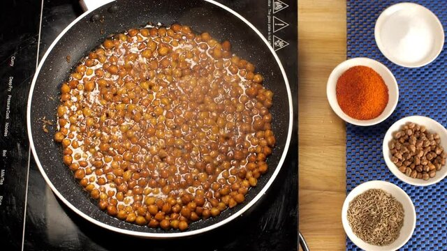 Small black Chana Sabzi/curry boiling in a non-stick pan - popular Indian recipe. Onion tomato gravy of spicy chickpea/Chana Masala preparation with raw ingredients placed on the blue mat