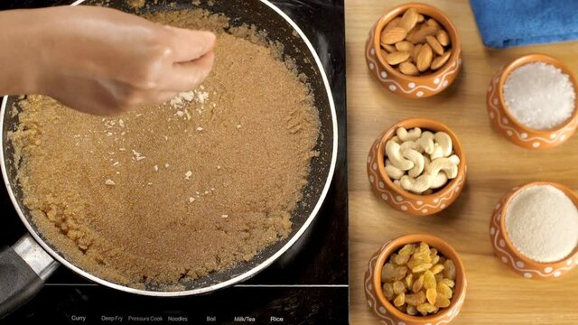 Grated dry fruits and raisins being dropped on top of freshly prepared Sooji Halwa. Closeup shot of delicious traditional Indian dessert cooking inside non-stick frying pan - Sheera/semolina pudding