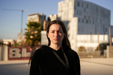 Fototapeta premium Looking to the camera. Portrait of a serious Hispanic young woman while standing in a city.