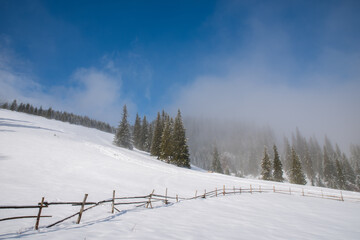 Long winding old wooden fence on a snowy hill in dense fog. Selective focus. Blurred background.