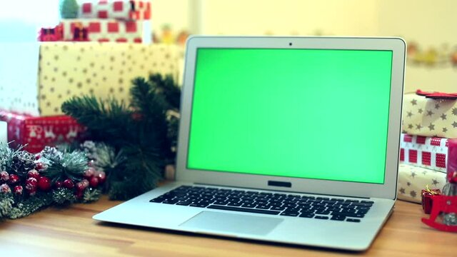Green screen laptop with Christmas decoration on background. New Year celebration concept. Presents for friends. Chromakey notebook. Free content. mockup monitor. Online greeting. Internet surfing. 
