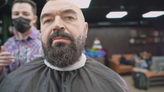 Barber applies cream to the cheeks of a bearded man.