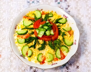 Salad in a plate, decorated with dill, cucumbers and tomatoes close-up against a white tablecloth
