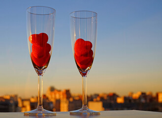 Couple glasses of champagne and red marmalade hearts on city view and blue sky background. Romantic mood. Copy space, selective focus