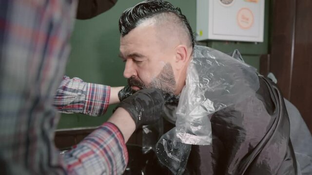 The hairdresser washes the paint off the man's beard