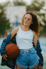 Beautiful young woman stands with ball among basketball playground.