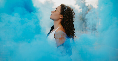 Portrait of young woman against background of blue smoke.
