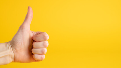Hand thumbs up sign on yellow background. Confirm gesture. Left side. Accept gesture and approve sign
