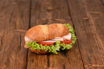 Sandwich with ham and fresh salad on the wooden table.