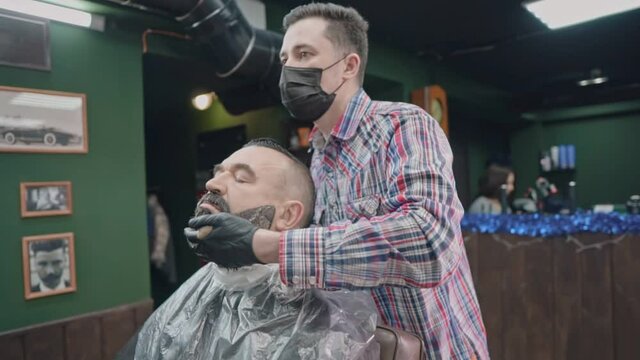 The barber spreads the paint on the client's beard