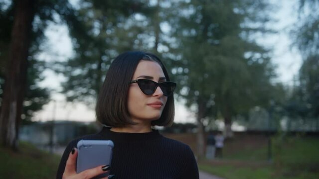 Beautiful young woman walks down the street with sunglasses looking at her phone