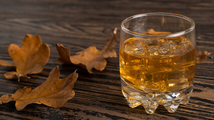 Glass of scotch whiskey and dried leaves. Autumn alcoholism. Brandy and dried oak leaves