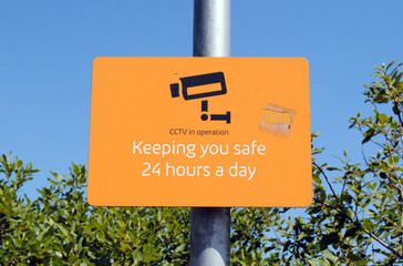Close Up of Orange Security Sign on Pole against Blue Sky  
