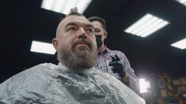 A bearded man sits on hair coloring in a barbershop.