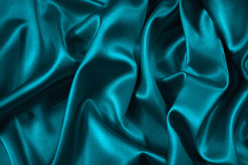 Blue green silk satin fabric. Teal color elegant background. Liquid wave or silk wavy folds. Beautiful dark turquoise background with copy space for your design.