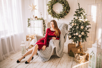 Beautiful cheerful happy young girl with christmas gifts on sofa on the background of a new year tree at home