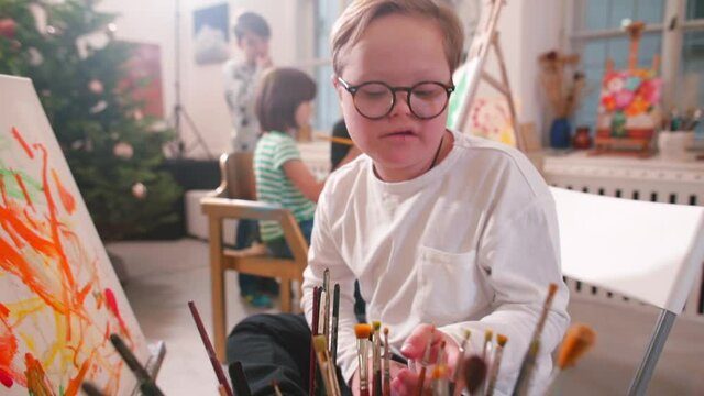 A 10-year-old child with Down syndrome is gifted with talents. Creativity is his outstanding ability. The boy talks about his strengths of personality, uses a palette with paints and the canvas.