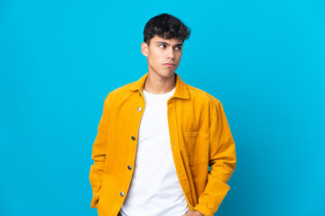 Young man over isolated blue background having doubts while looking side