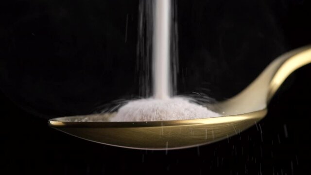 pouring collagen powder in golden spoon on black background closeup. Natural beauty and health supplement